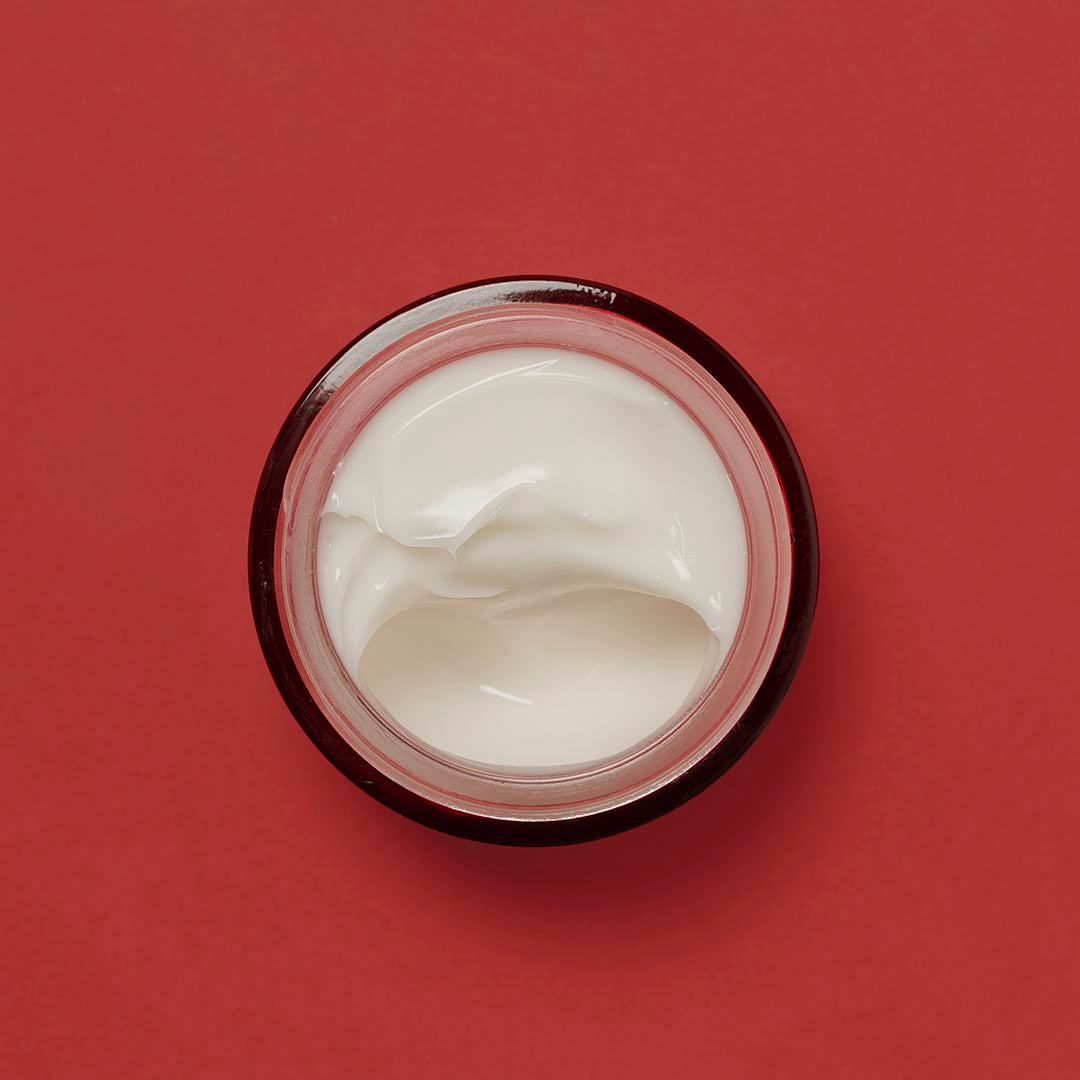 Textura_de_crema_skin_k_pause_cream_en_tarro_abierto_sobre_fondo_rojo