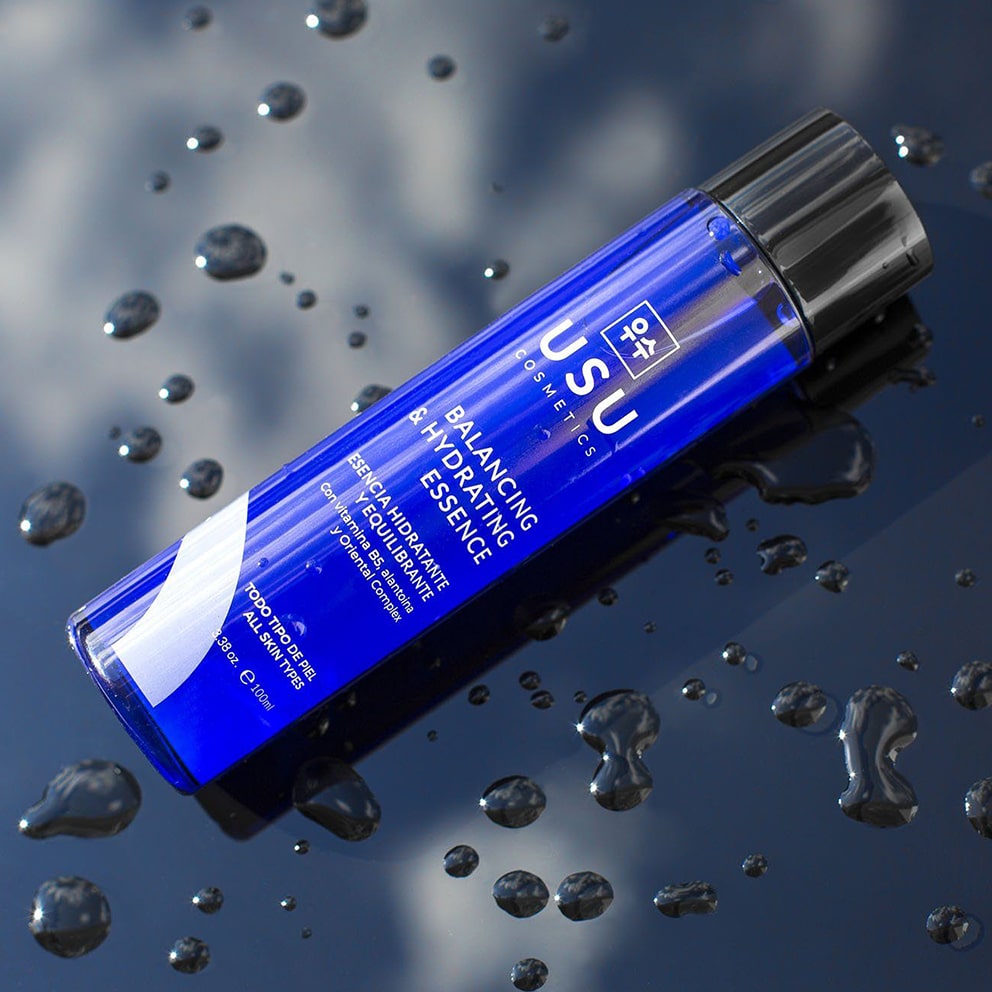 Bote de 100ml de esencia coreana hidratante y equilibrante sobre superficie con gotas